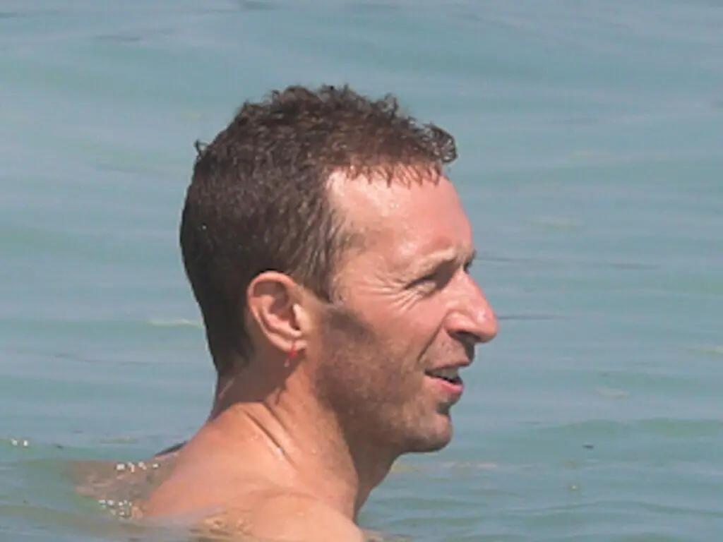 Chris Martin, do Coldplay, exibe peitoral definido na praia e impressiona